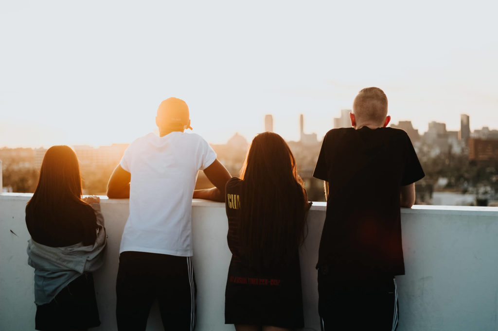 Fyra ungdomar står och tittar ut över en stad i solnedgången